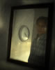 Reflection of a man in checkered work shirt in a mirror, he's looking down, and a clock on the wall is beside him in the reflection: time is 4:20; the shadow of his shoulder is to the left of the image, and the whole has a scratchy veneer