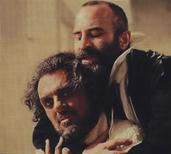 Iago from behind hugs Othello around his neck