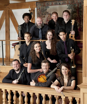 The tour troupe sitting in the wooden Blackfriars theater, most holding instruments.