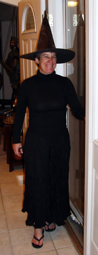 Sarah in a witch's hat and long black dress standing in the front door entryway of our house