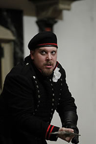 Richard in uniform and beret with sword pointed toward camera